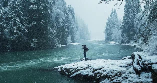 A man in winter clothing standing on a rock in a snowy river